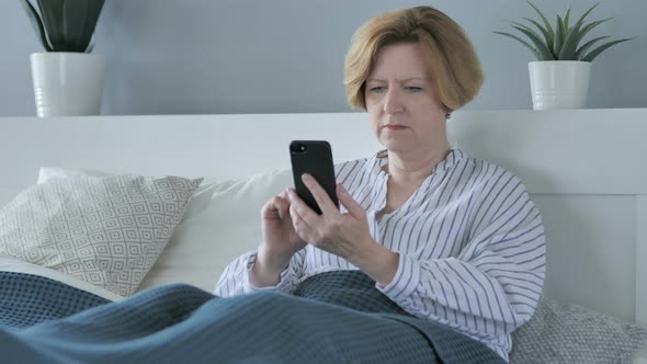 Old Senior Woman Using Smartphone while Lying in Bed