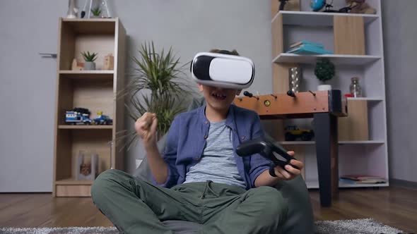 Boy which Playing Video Game on the Bean Bag Sofa Using Virtual Reality Headset