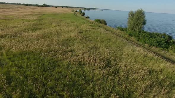 FPV Drone Racing View. Fly Over Coastline with Field and Dirt Road