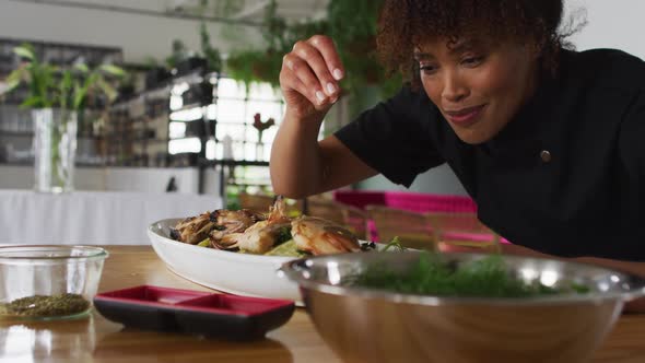 Mixed race female chef preparing a dish and smiling in a kitchen