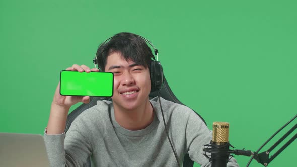 Man With Headphone Showing Green Screen Mobile Phone While Sitting In Front Of Green Screen