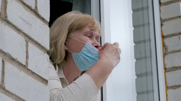 Woman Looks Out Of Window And Removes Mask From Face Taking Breath Of Fresh Air