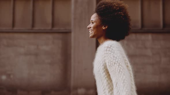 Smiling Young Woman With Windswept Afro Hair Walking Along Street