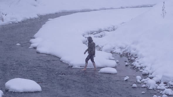 A man crossing the stream barefoot in the snow.