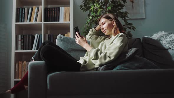 Positive Woman Resting on Couch with Smartphone