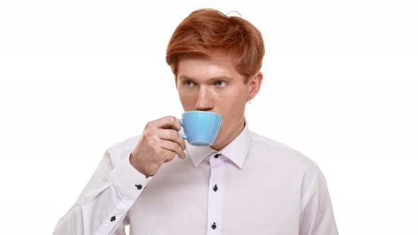 Young Caucasian Redhead Man Drinking Coffee From Blue Cup and Showing Ok on White Background