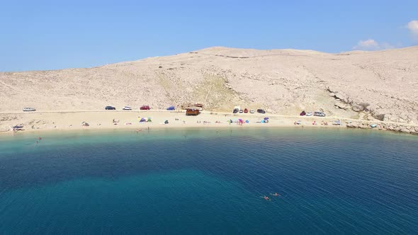 Flying above umbrellas and people on isolated beach of Pag island, Croatia