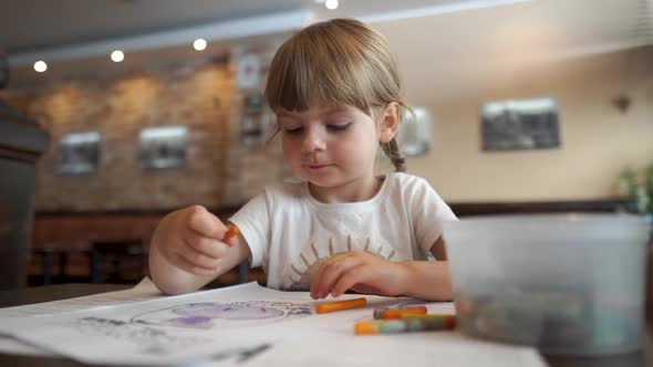 Little Happy Girl Coloring a Picture in a Cafe