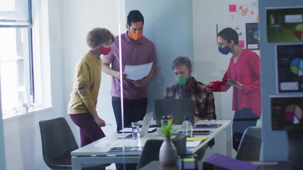 Diverse colleagues wearing face masks working together in meeting room at modern office