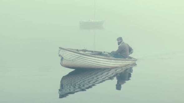 Man in fiberglass rowboat spins boat within fog