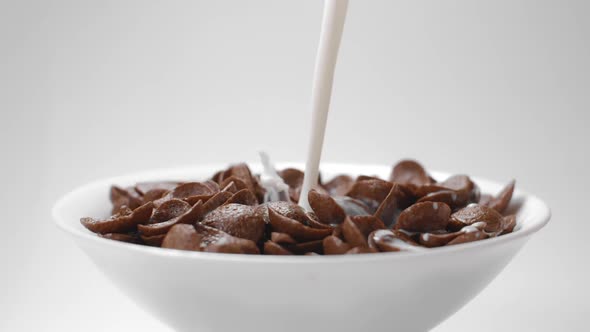 Milk Is Poured To the Bowl with Chocolate Corn Flakes in Slow Motion, Drops of Milk Falling in