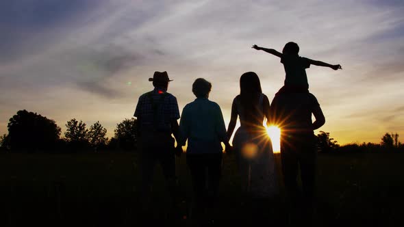 Three Generation Family Walk in Meadow at Sunset