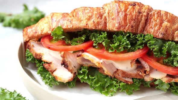 Croissant sandwich with meat, vegetables and green kale, white background. 