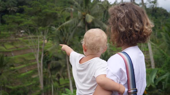 Back View of a Caucasian Woman Holding Her Baby Looking at the Jungle Landscape