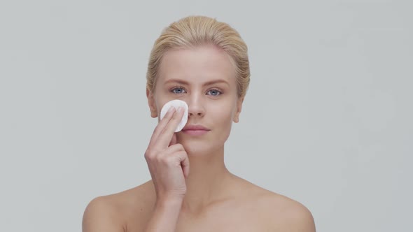 Studio portrait of young, beautiful and natural blond woman applying skin care cream. F