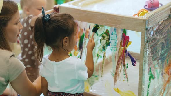 a Cute Little Girl Painting on the Glass in the Kindergarten