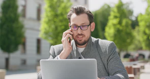 Young Man Wearing Glasses with Mustaches and a Beard is Sitting at the Table in the Square is