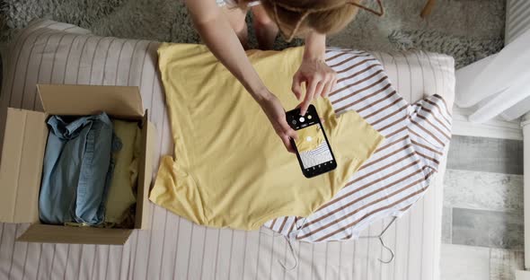 Woman taking picture with phone of used clothes to sell online.