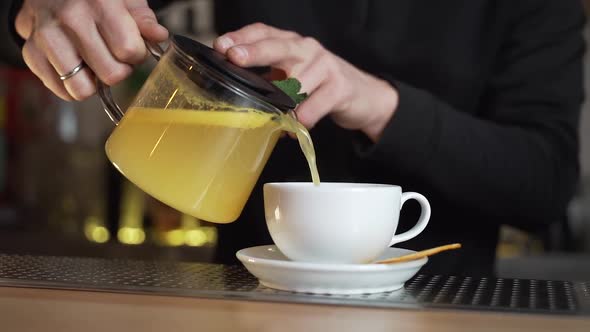 Bartender pours green herbal tea into white cup at bar counter