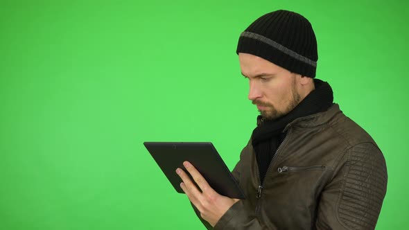 A Young Man in a Winter Outfit Works on a Tablet, Then Smiles at the Camera - Green Screen Studio