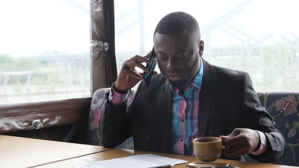 Afro American Businessman is Calling on Smartphone and Drinking Coffee in Cafe