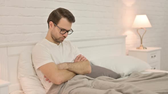 Drowsy Young Man Falling Asleep Sitting in Bed