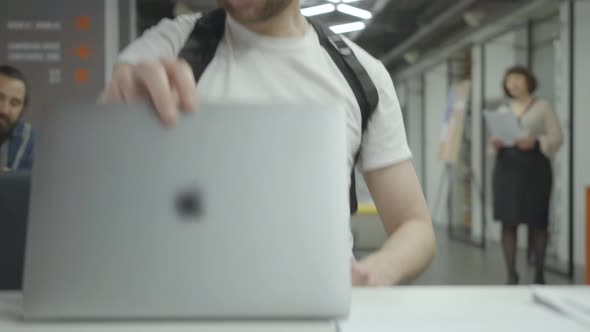 Confident Young Man in White T-shirt Working with Laptop Sitting at the Table in the Modern Office