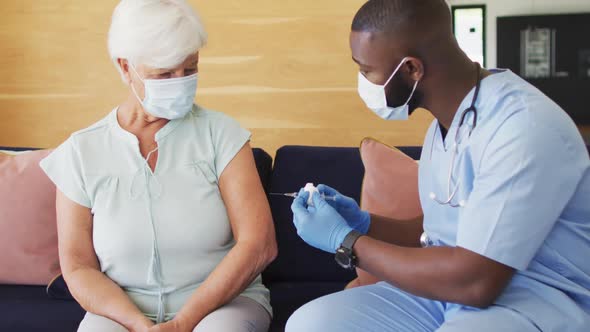 Video of african american male doctor in face mask vaccinating caucasian senior woman