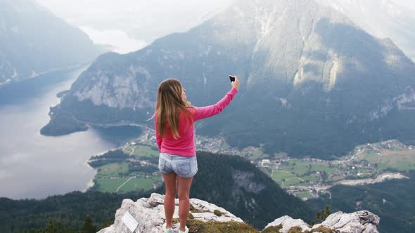 Young Woman Taking Photo with Smart Phone at Mountain Peak Wth Stunning Mountain Lake Background