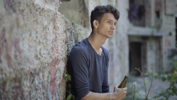 Side View of Desperate Gypsy Man Drinking Beer at Urban Slum. Portrait of Depressed Young Guy with