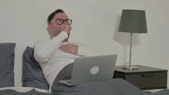 Casual Man Coughing While Using Laptop in Bed