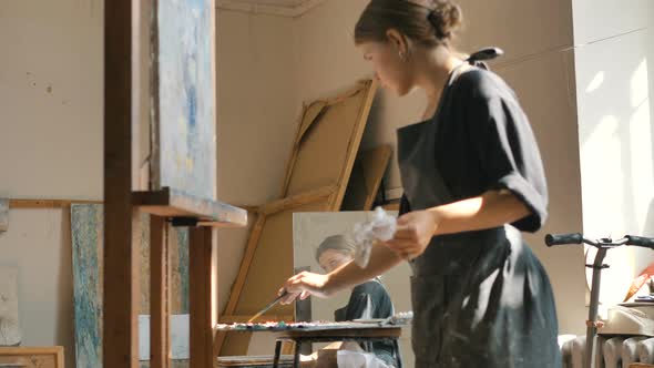 Woman Draws Picture with Brush Near Palettes and Mirror