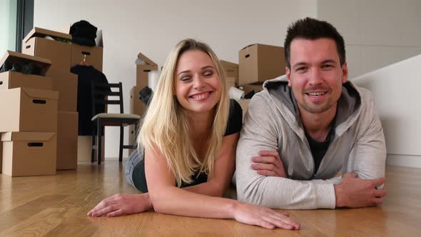 A Happy Moving Couple Lies on the Floor of an Empty Apartment and Talks To the Camera with a Smile