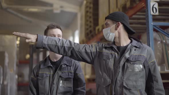 Two Caucasian Men in Face Masks Discussing Work Plan in Warehouse, Portrait of Professional Male