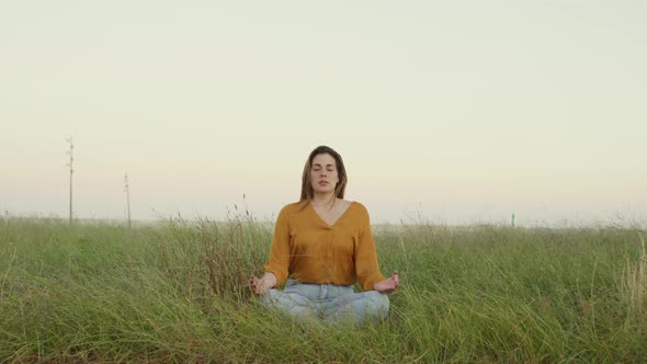 Young woman sitting on a meadow and meditating in the evening