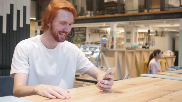 Video Chat on Smartphone By Redhead Beard Man in Cafe