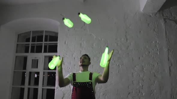 Young Handsome Male Bartender Juggling with Green luminous Bottles