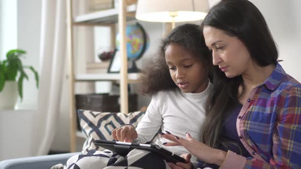 Mother and Brunette Kid Is Sitting on Sofa and Using Electring Digital Technology