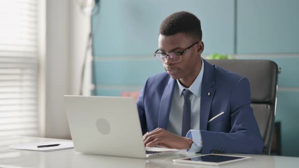 Young African Businessman Looking at Camera While Using Laptop in Office