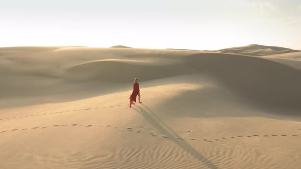  Aerial View of a Girl in Fluttering Red Dress Walking on Sand Dunes at Sunset