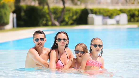 Happy Family of Four in Outdoors Swimming Pool