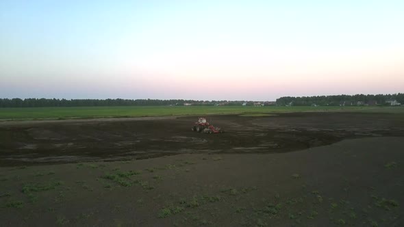 Tractor Plows Field with Harrow at Green Meadow Aerial View