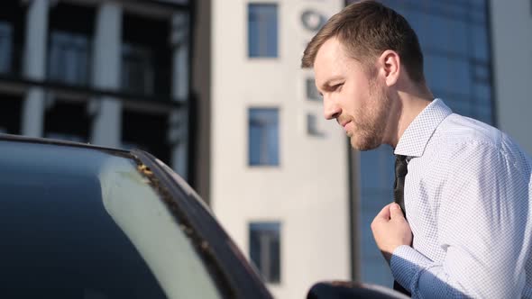 Businessman Puts on a Tie on the Street Looking Out the Window of His Car