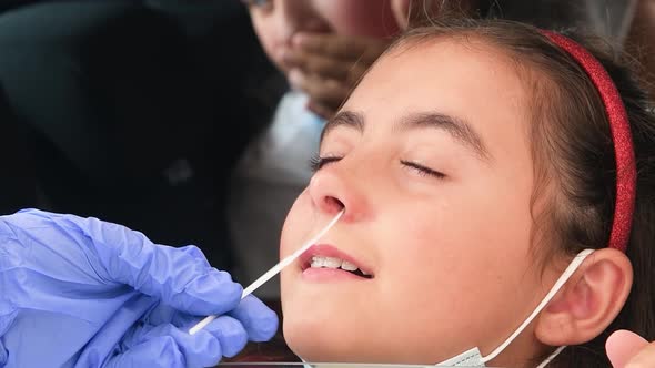 Pediatrician Taking Nasal Mucus Test Sample From Elementary Age Girl's Nose Performing Respiratory