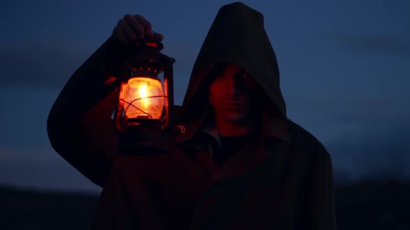 a Man of Caucasian Nationality in a Dark Green Raincoat with a Luminous Lantern the Evening Season