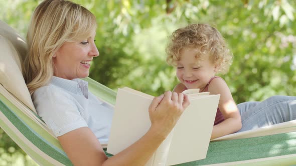 happy mothers day, smiling mom reading story from the book to her blue eyed little girl daughter chi