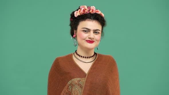 Studio Portrait of Frida Kahlo Lookalike Woman in Mexican Dress Wearing Jewelry and Roses in Hair