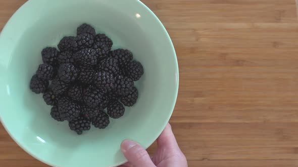 A woman's hand putting a bowl full of blackberries on a cutting board, removing them again