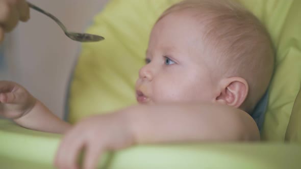 Mother Feeds Little Son with Puree in Comfortable Highchair