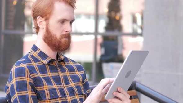 Beard Young Man Using Tablet while Sitting Outdoor